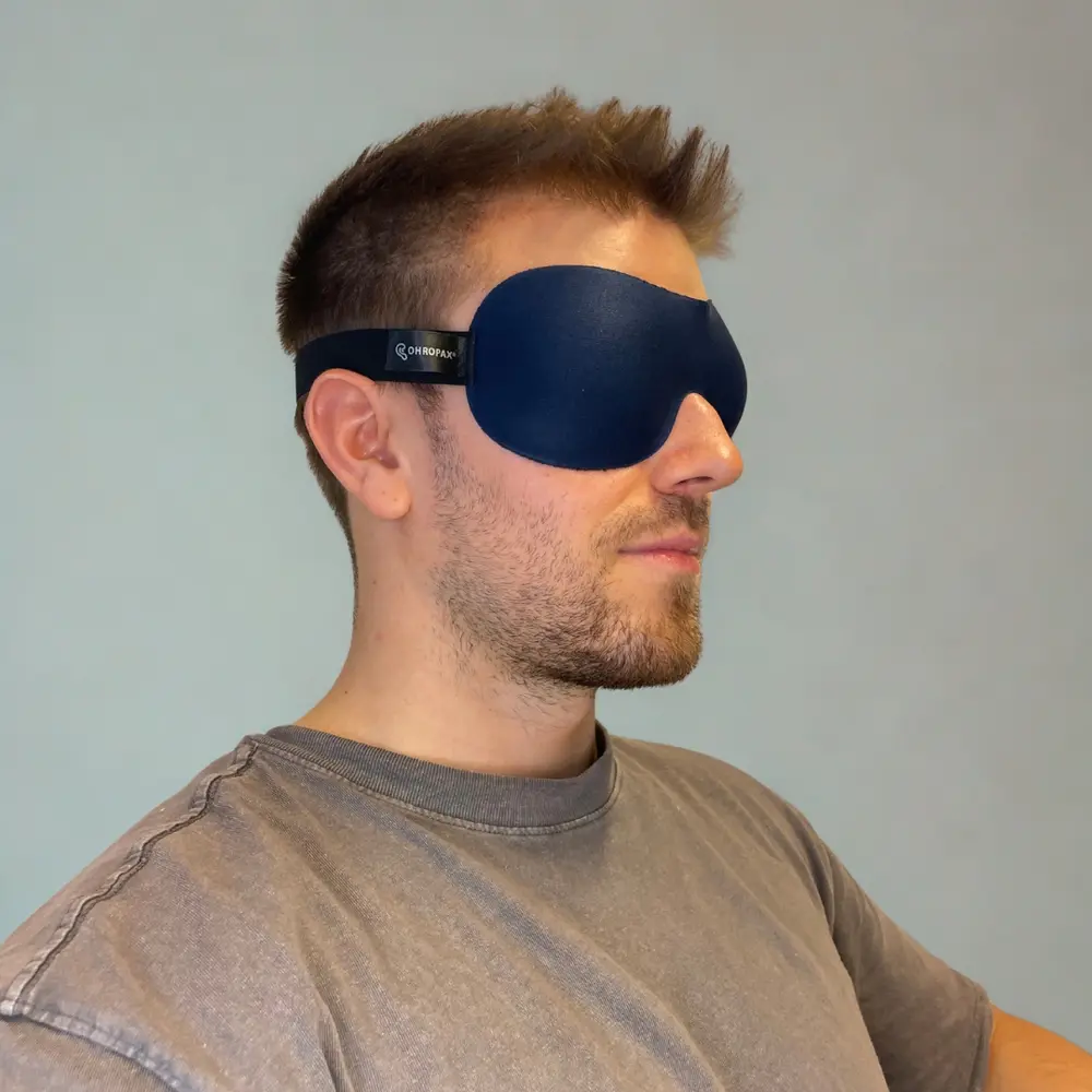 Mann mit OHROPAX 3D Schlafmaske in Seitenansicht, vor hellblauem Hintergrund