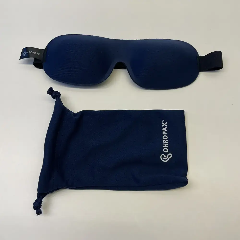 OHROPAX Schlafmaske und dunkelblauer Stoffbeutel mit Logo nebeneinander auf weissem Tisch